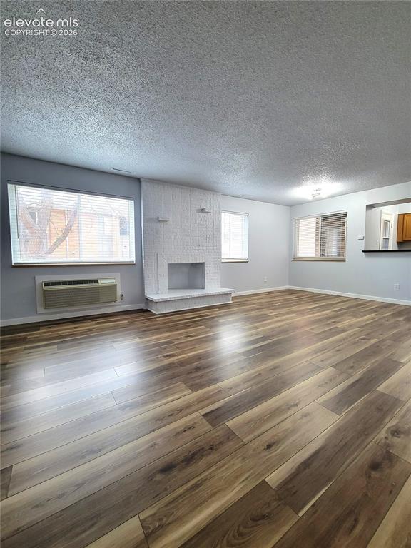 Image 5 of 32: Spacious living area featuring wood-finish flooring, a white brick fireplac