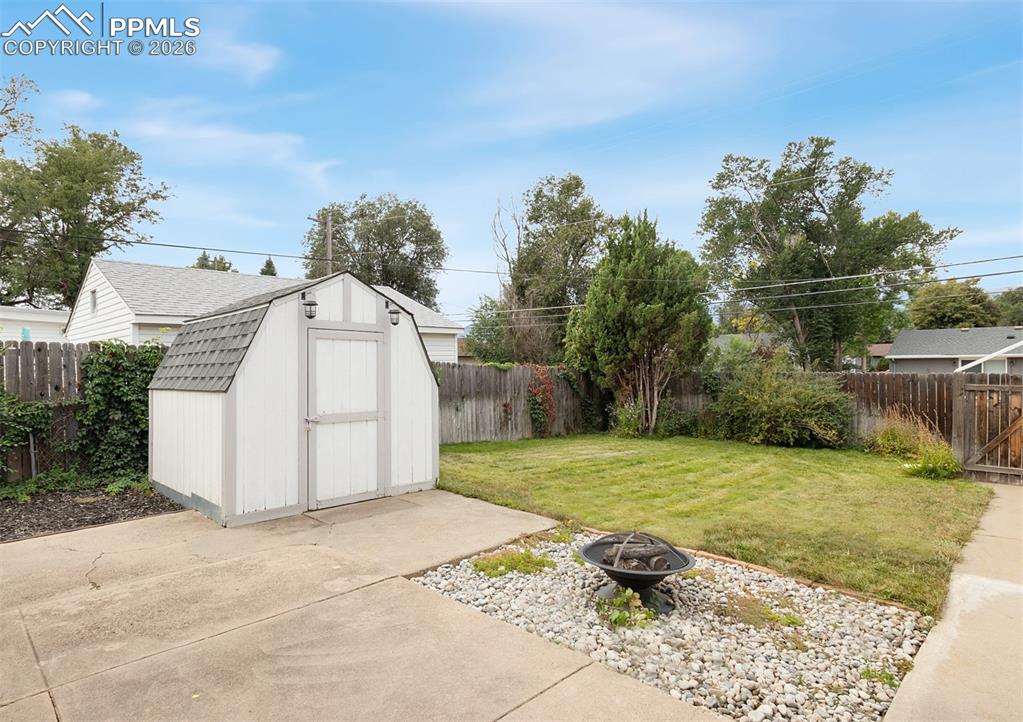 Image 16 of 20: Inviting back yard with large covered patio, firepit, lawn, cute shed, and 