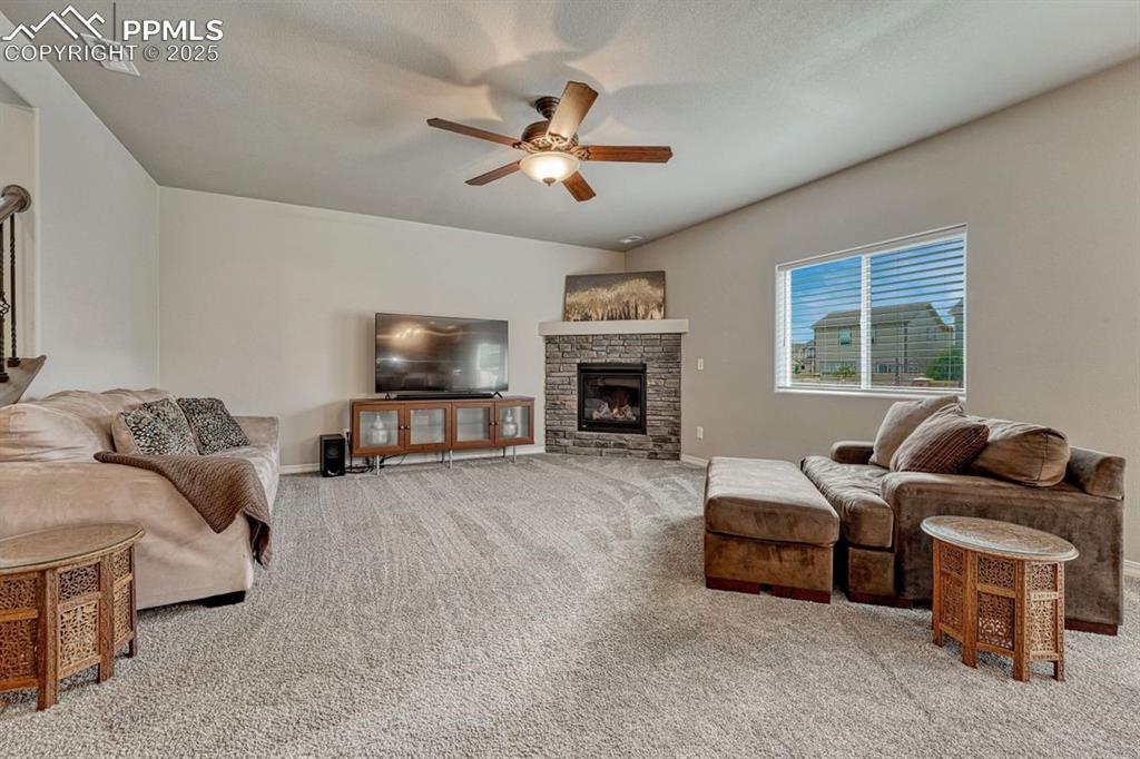 Image 2 of 40: Spacious great room with stone surround gas fireplace, ceiling fan and west