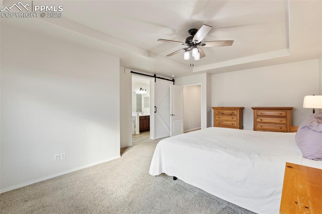 Image 13 of 31: Bedroom with a raised ceiling, light colored carpet, a barn door, ceiling f