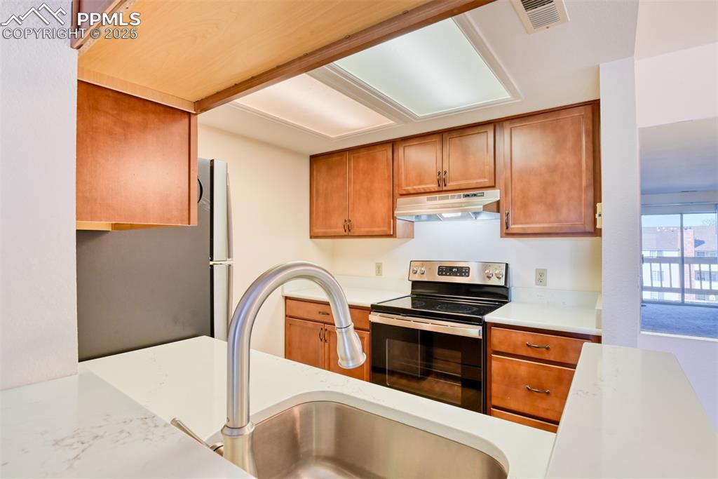 Image 14 of 42: Kitchen featuring stainless steel appliances, brown cabinets, under cabinet