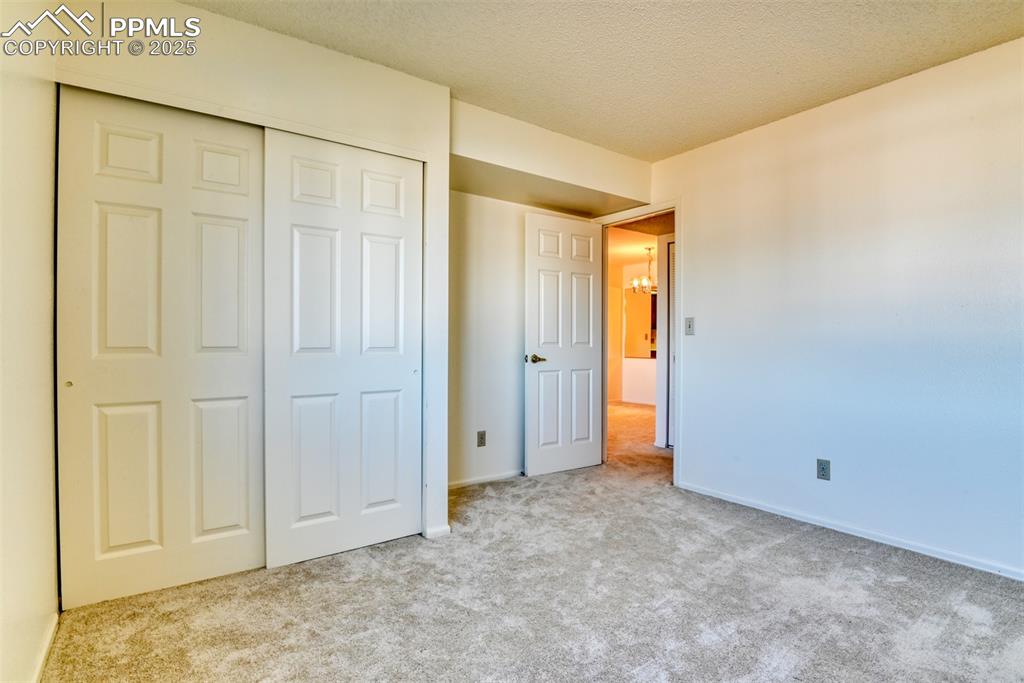 Image 32 of 42: Unfurnished bedroom with light colored carpet, a closet, and a textured cei