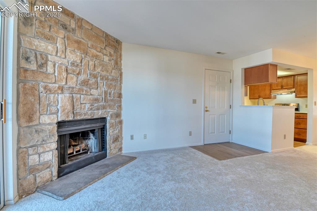 Image 7 of 42: Unfurnished living room featuring light colored carpet and a stone fireplac