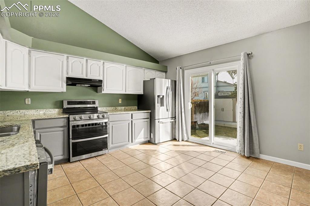 Image 6 of 20: Kitchen with stainless steel appliances, light stone counters, white cabine