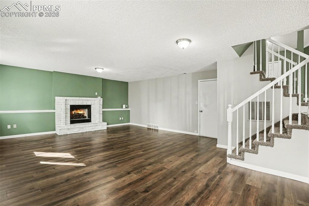 Image 7 of 20: Unfurnished living room featuring dark wood-style floors, a brick fireplace