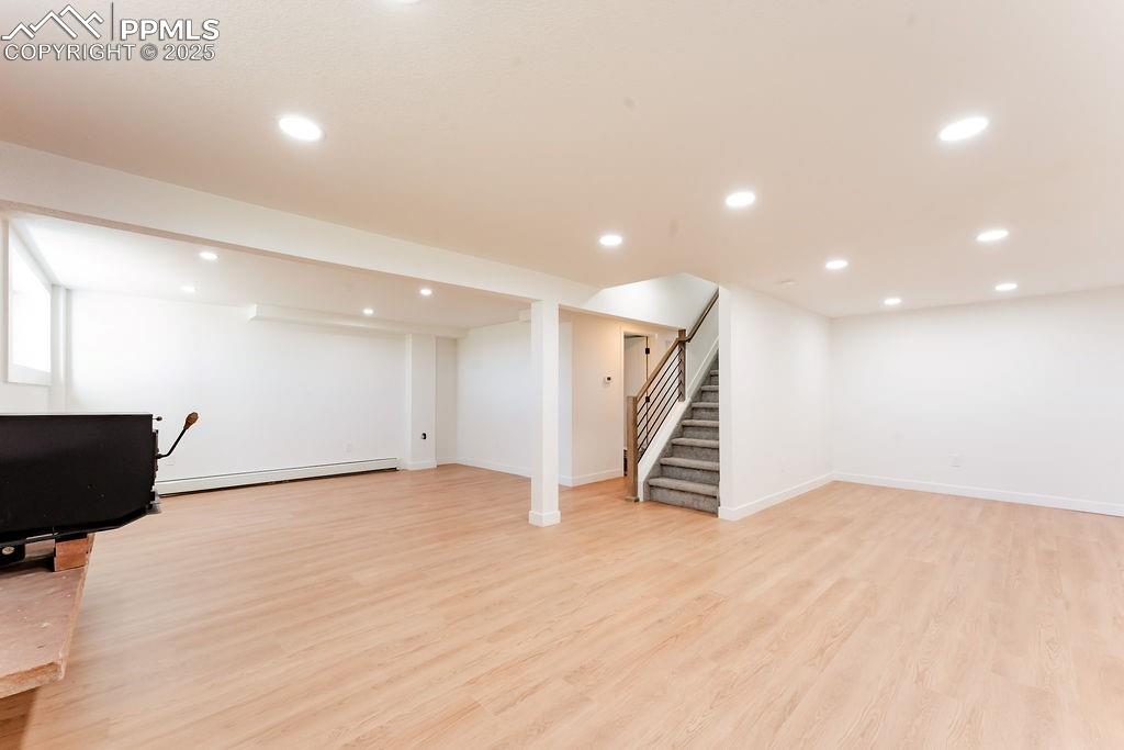 Image 34 of 43: Finished basement with light wood-style flooring, recessed lighting, stairw