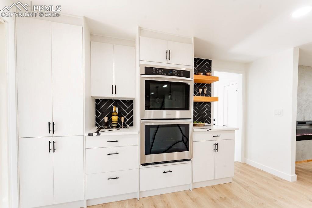 Image 7 of 43: Kitchen featuring double oven, white cabinets, open shelves, light countert