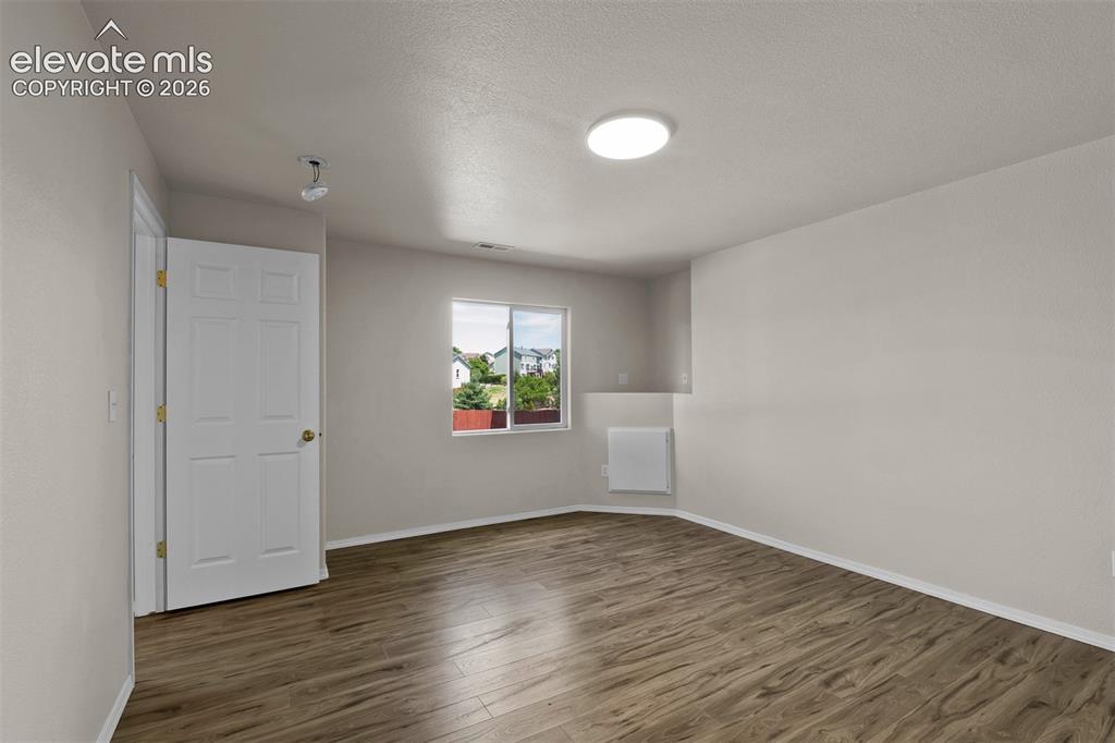 Image 29 of 46: Spacious room with wood-finish flooring, a contemporary ceiling light fixtu