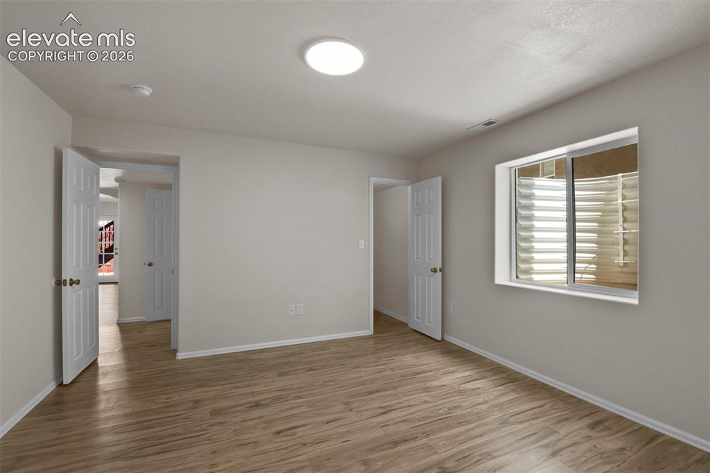Image 32 of 46: Spacious room featuring wood-finish flooring, light neutral wall tones, and