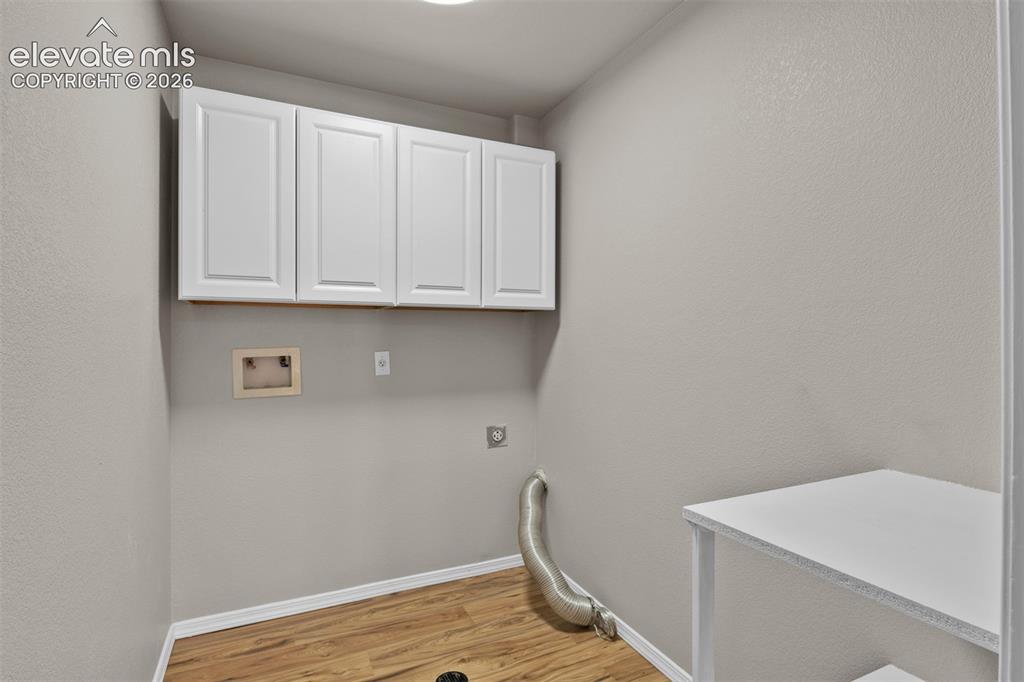 Image 35 of 46: Laundry area featuring wood-finish flooring, overhead white cabinetry, and