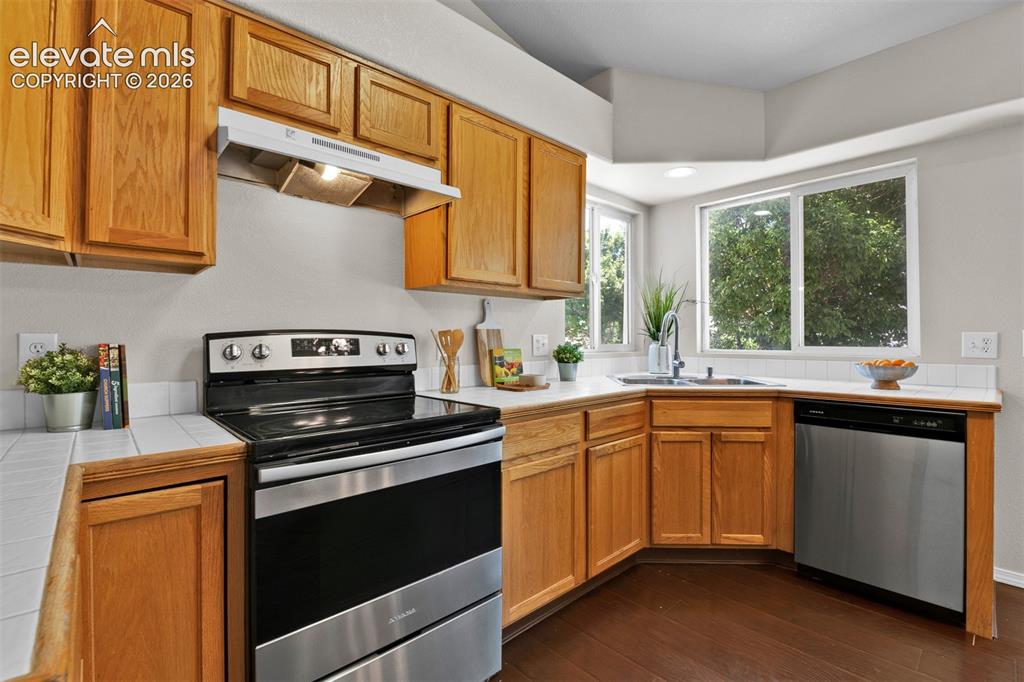 Image 6 of 46: Kitchen featuring wood cabinetry, white tile countertops, stainless steel a