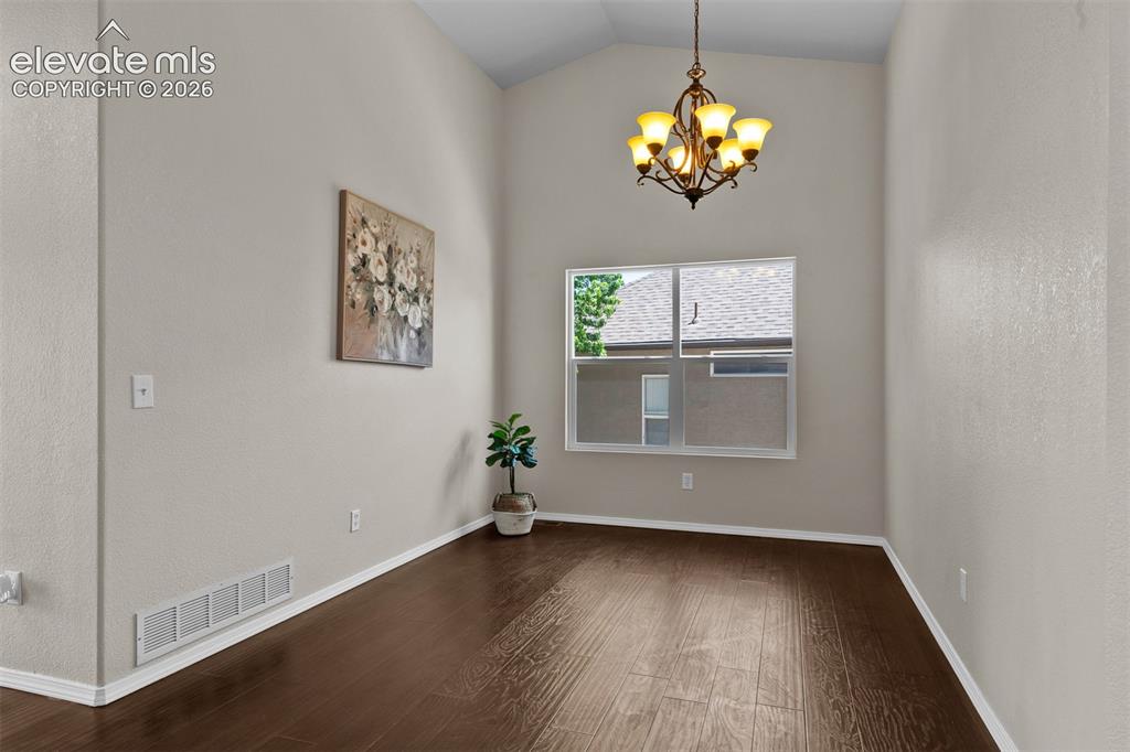 Image 9 of 46: Vaulted ceiling space featuring wood-finish flooring, a decorative chandeli