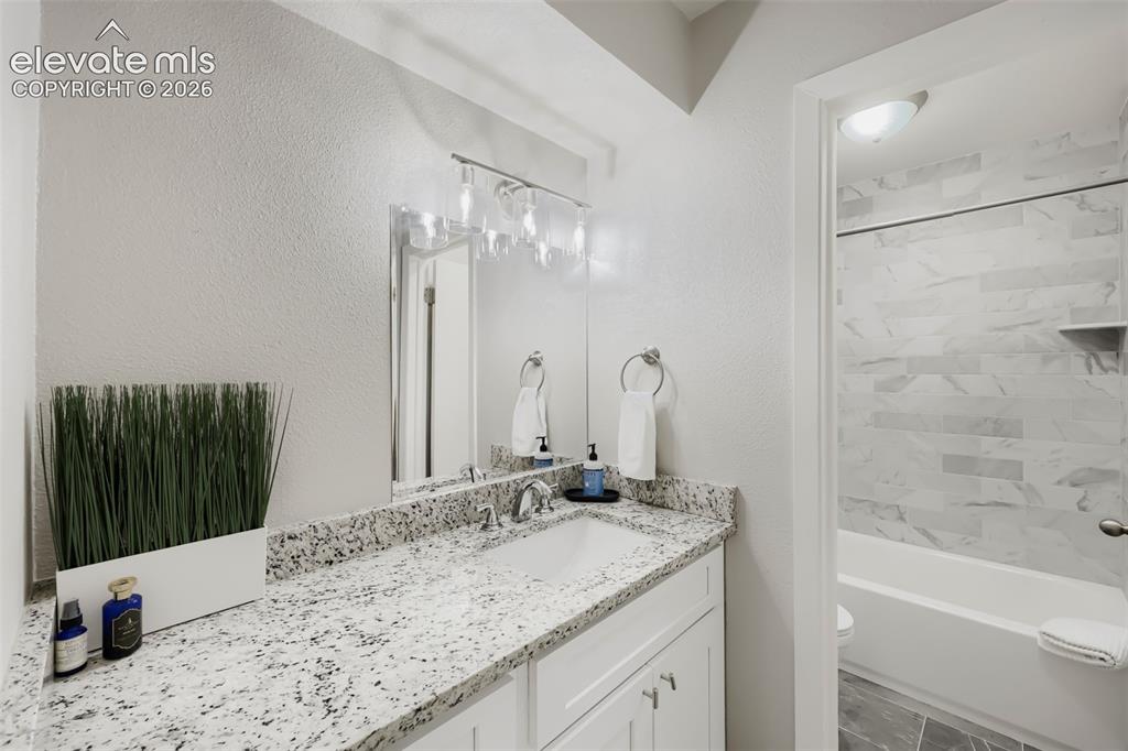 Image 12 of 28: Bathroom featuring a white vanity with a light-colored speckled countertop,