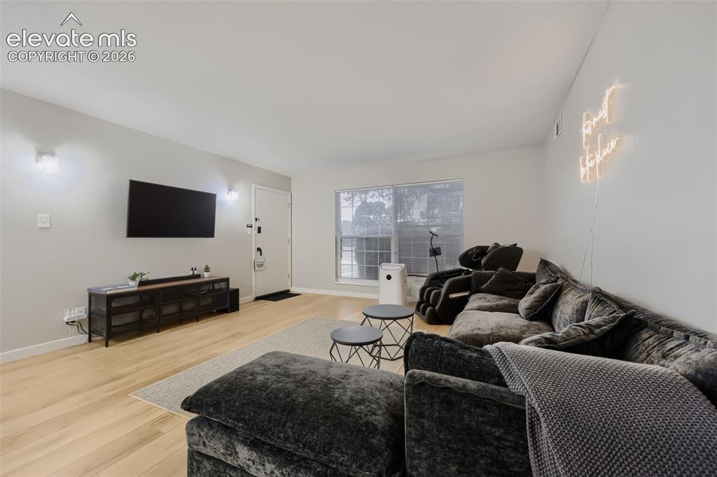 Image 14 of 28: Open-concept living area with light wood-finish flooring, white walls, and