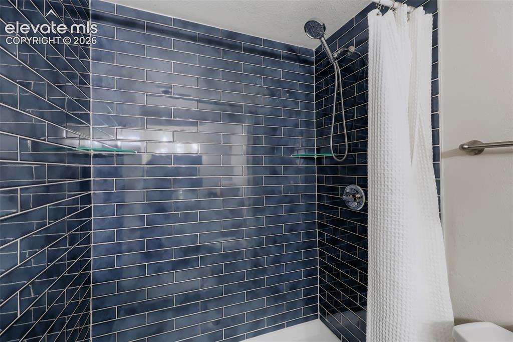 Image 7 of 28: Shower featuring deep blue subway tile, chrome fixtures, and built-in glass