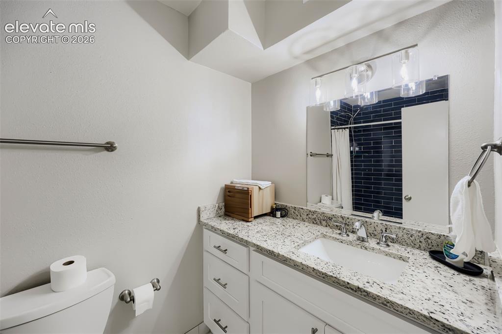 Image 8 of 28: White vanity with a speckled countertop, undermount sink, and chrome faucet