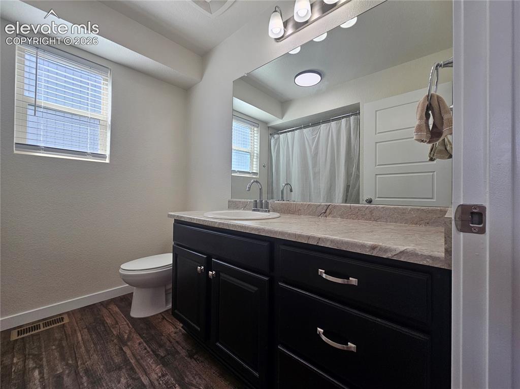 Image 12 of 23: Dark wood-finish flooring with a white toilet and window