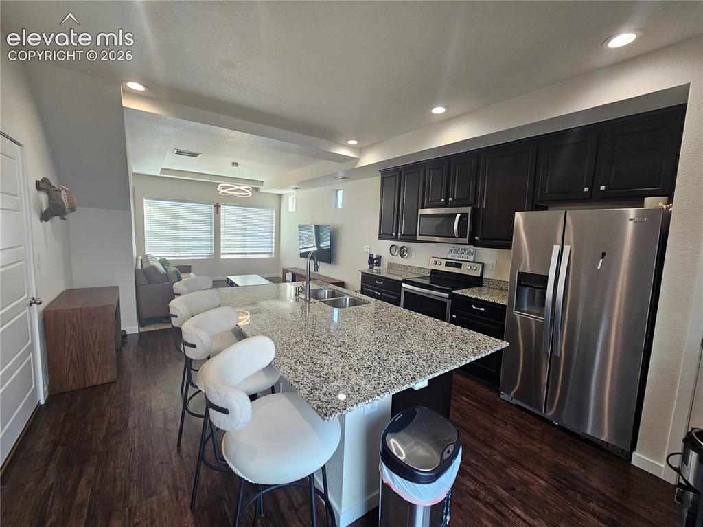 Image 8 of 23: Kitchen featuring dark cabinetry, stainless steel appliances, a multi-level