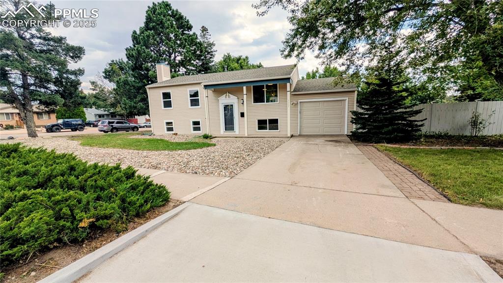 Caption: Split foyer home featuring concrete driveway, an attached garage, a chimney, and roof with shingles
