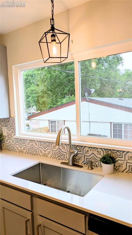 Image 36 of 39: Kitchen view of backsplash, light stone counters, and decorative light fixt