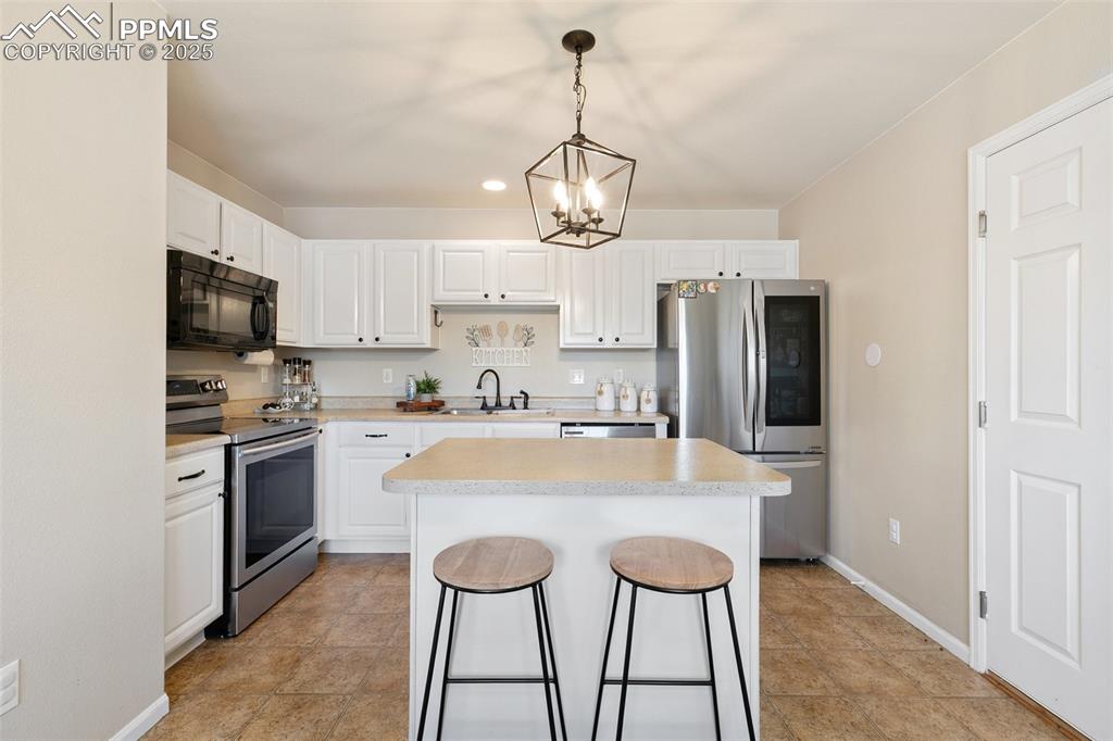 Image 10 of 27: Kitchen with stainless steel appliances, a chandelier, white cabinetry, lig