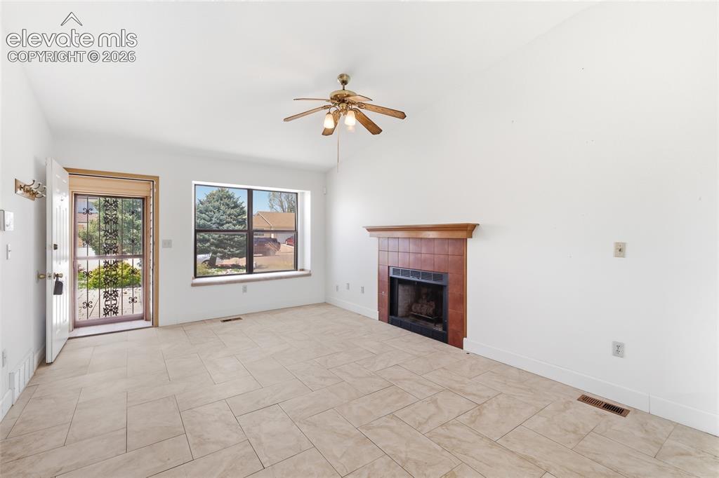 Image 6 of 29: Living area featuring light-toned tile flooring, a fireplace with a wood ma