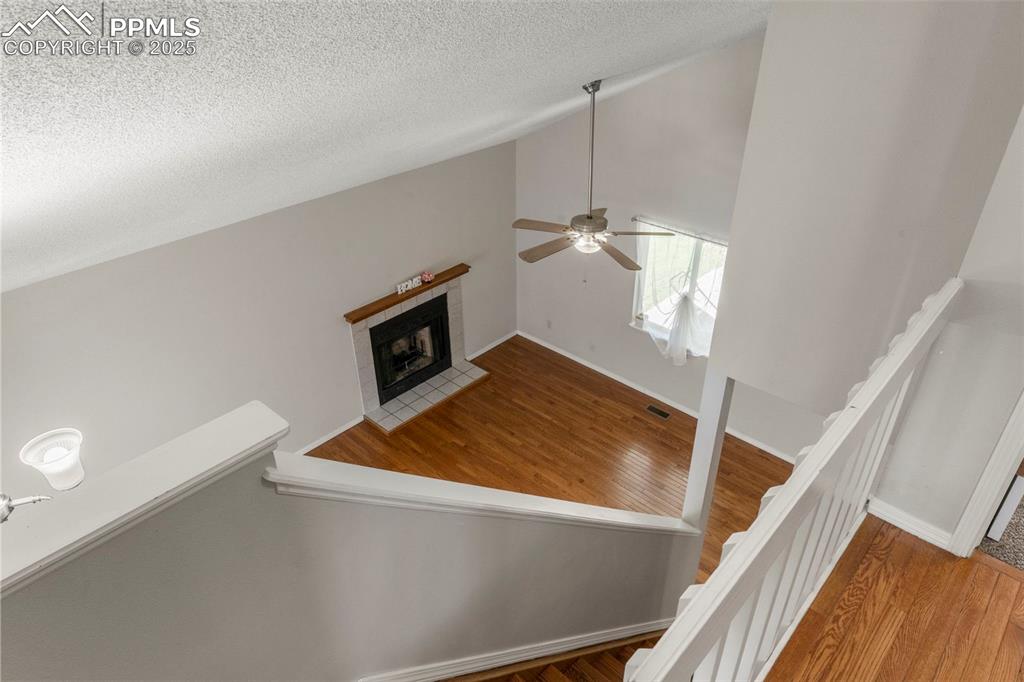 Image 19 of 24: Staircase with a tiled fireplace, vaulted ceiling, wood finished floors, an