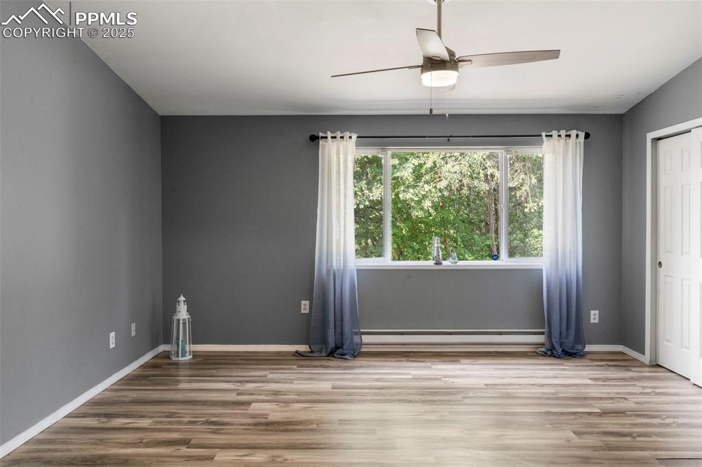 Image 9 of 24: Spare room with wood finished floors, a ceiling fan, and a baseboard radiat