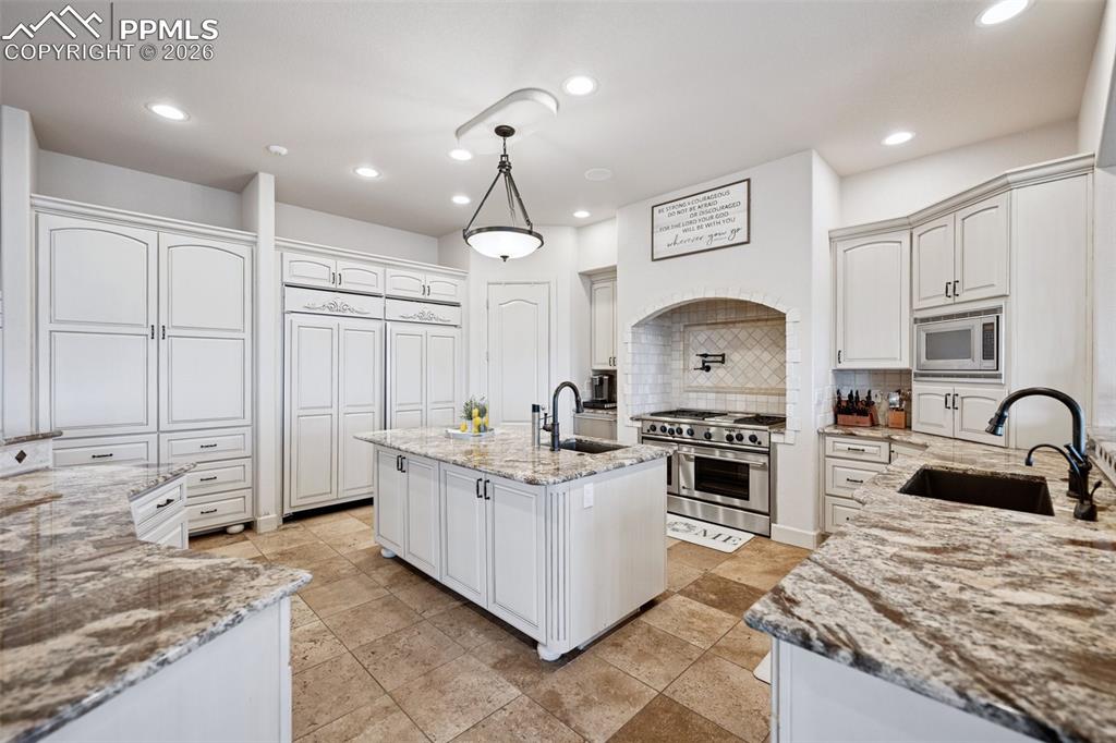 Image 16 of 50: Kitchen with stainless steel appliances, a sink, backsplash, and light ston