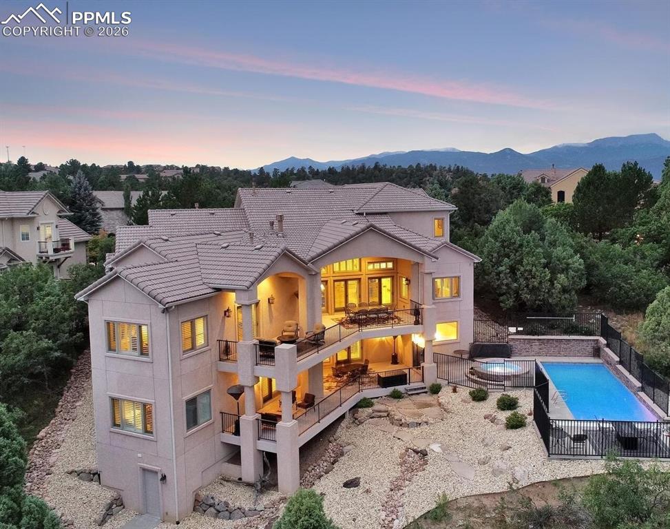 Image 3 of 50: Back of property at dusk featuring a balcony, a tiled roof, fence, a mounta