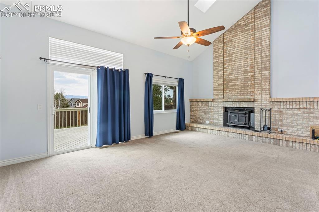Image 11 of 37: Unfurnished living room with a wood stove, carpet flooring, high vaulted ce