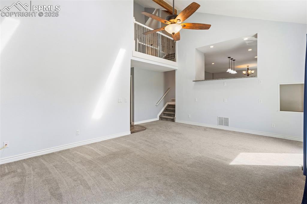 Image 12 of 37: Unfurnished living room with high vaulted ceiling, carpet, a ceiling fan, s