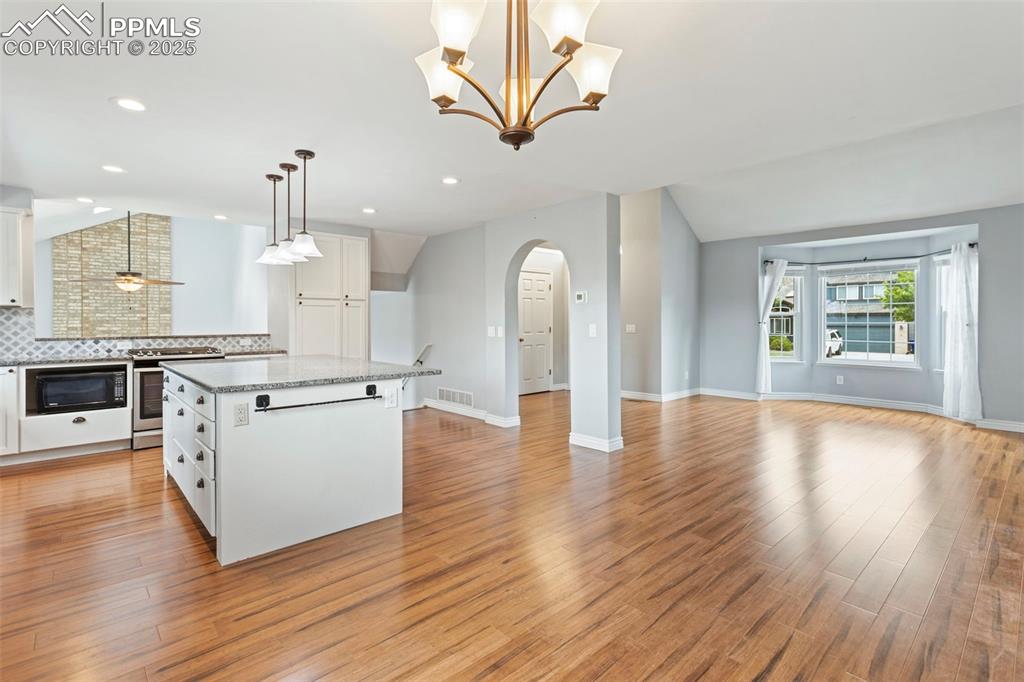 Image 7 of 37: Kitchen featuring white cabinetry, lofted ceiling, pendant lighting, arched