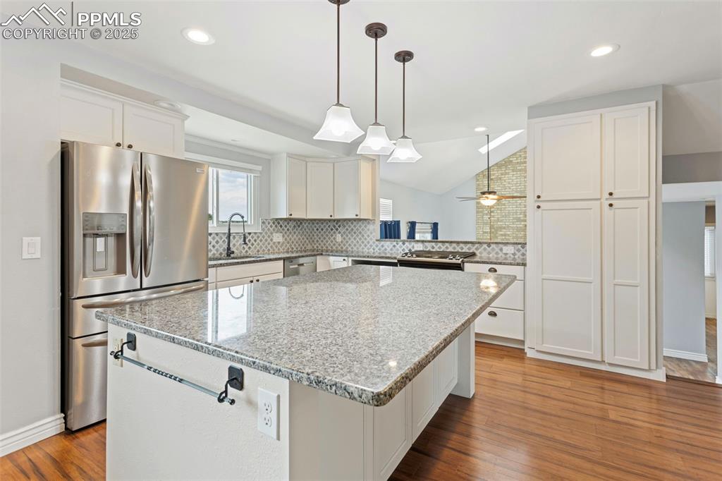 Image 8 of 37: Kitchen with stainless steel appliances, white cabinetry, vaulted ceiling,