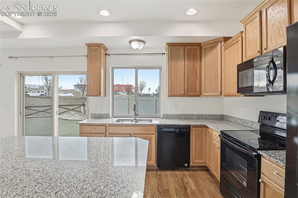 Image 4 of 29: Kitchen featuring black appliances, light stone countertops, light wood-typ