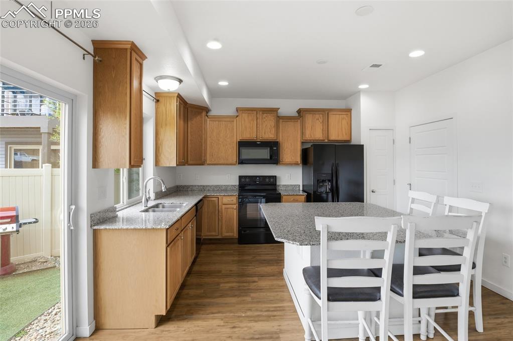 Image 9 of 29: Kitchen with black appliances, light stone countertops, a kitchen island, l