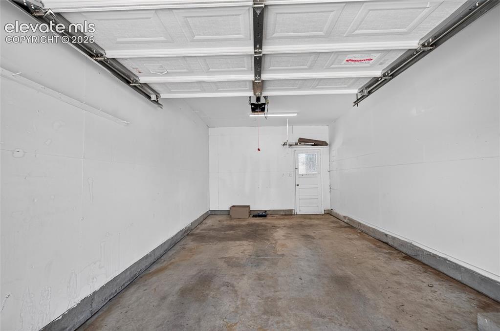 Image 19 of 21: Garage interior with white painted walls, concrete flooring, and an overhea
