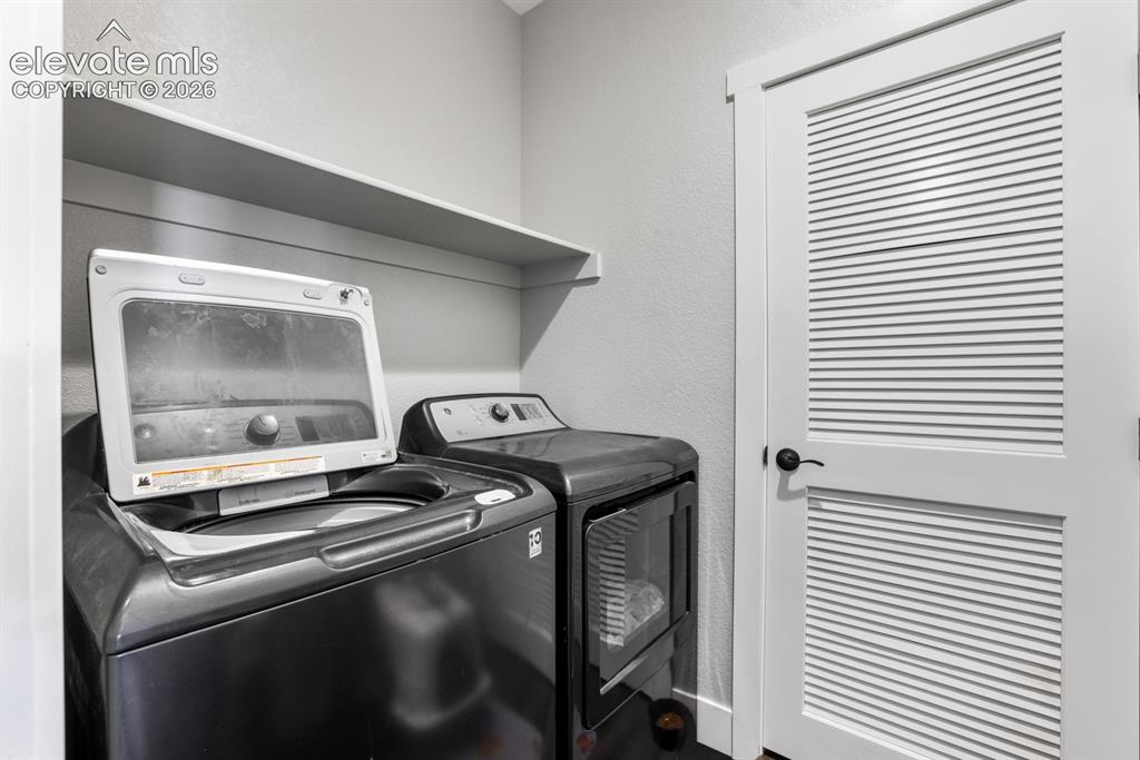Image 25 of 50: Dedicated laundry area featuring a built-in shelf, textured walls, and a lo