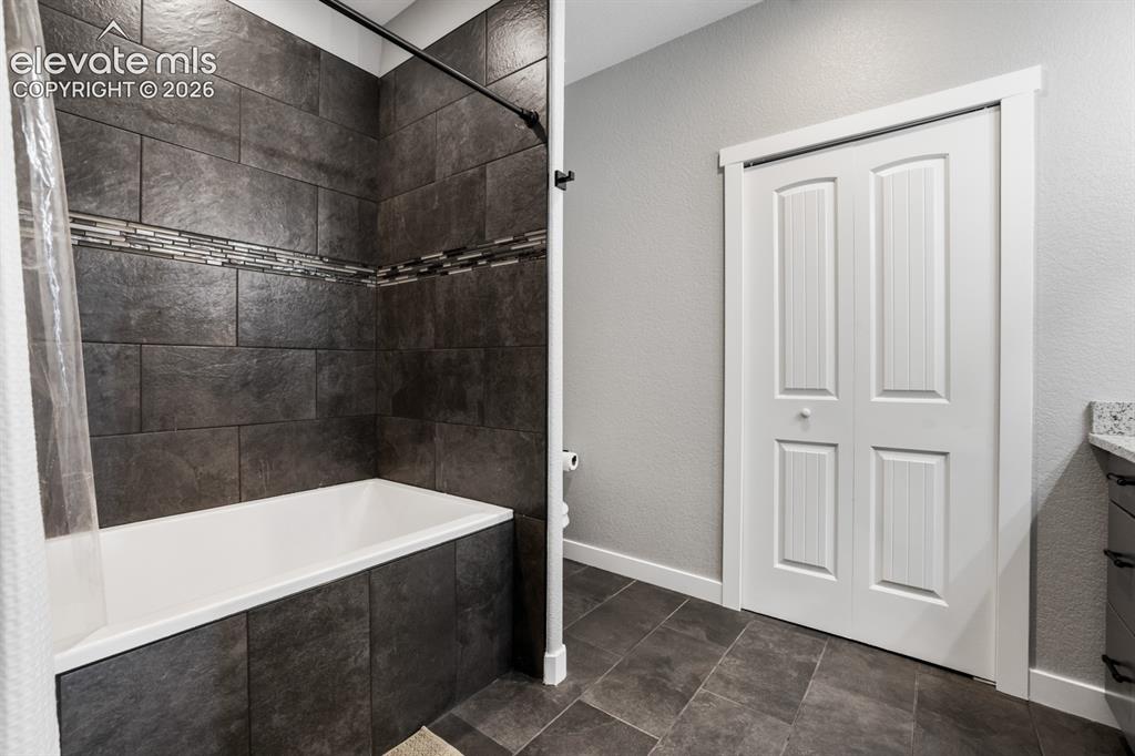 Image 26 of 50: Bathtub with dark rectangular tile surround and decorative mosaic accent ba