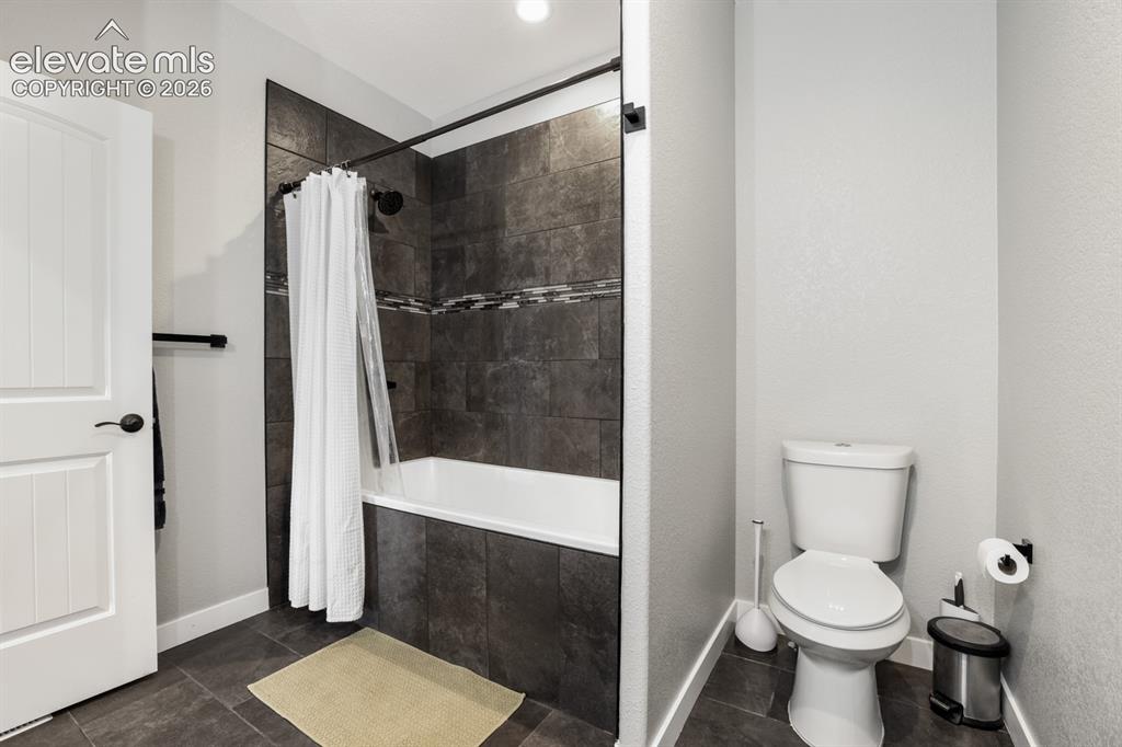 Image 27 of 50: Bathroom featuring a white bathtub and shower with dark tile surround, acce