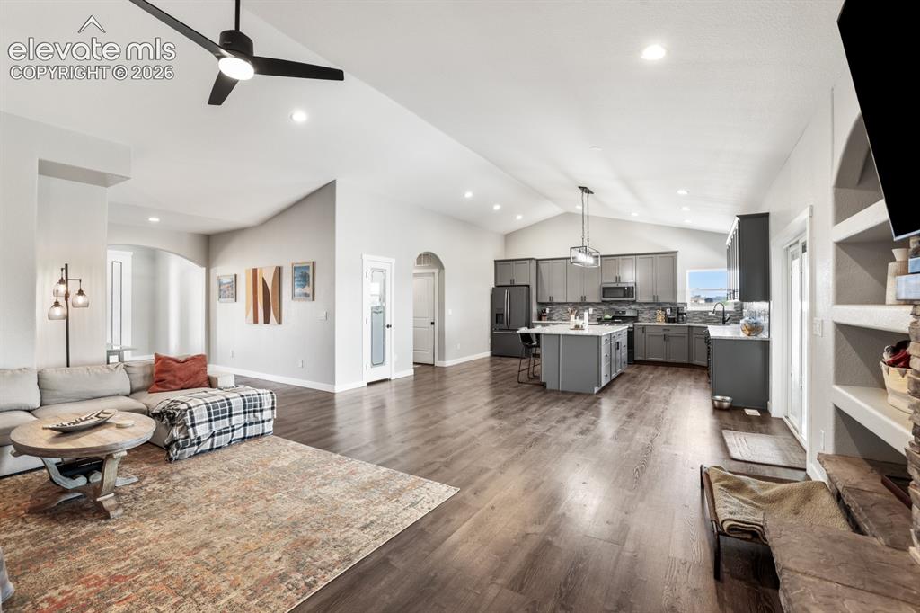 Image 6 of 50: Expansive living area featuring vaulted ceilings, wood-finish flooring, and