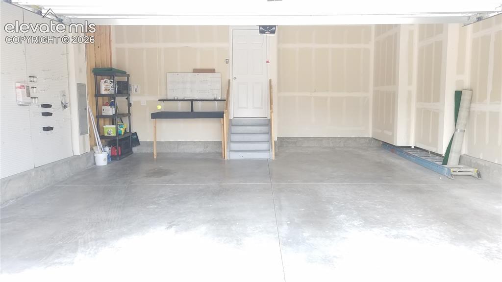 Image 24 of 32: Spacious garage with an exposed aggregate concrete floor, unfinished drywal