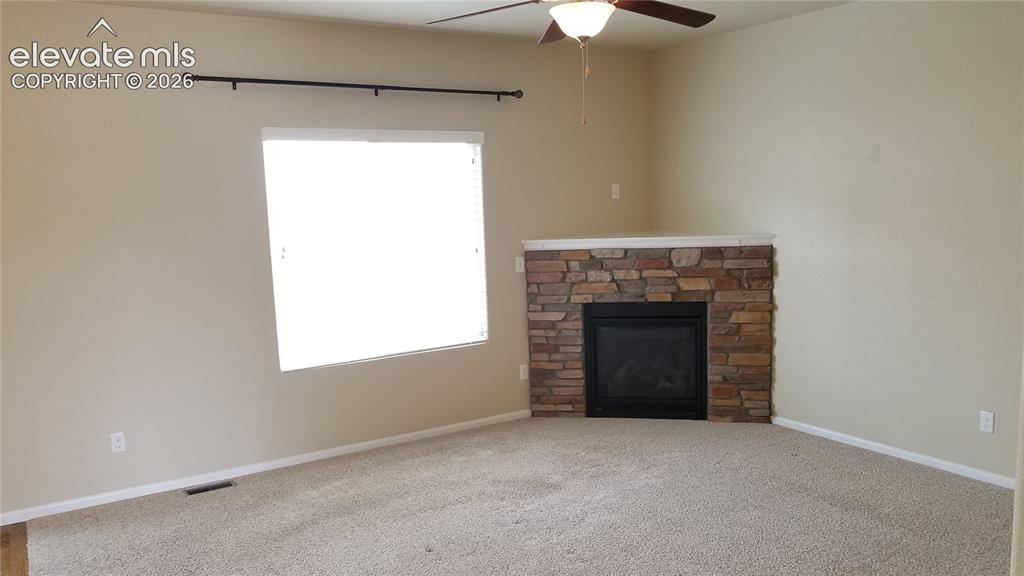 Image 6 of 32: Corner fireplace with stone surround and white mantle, carpet flooring, and