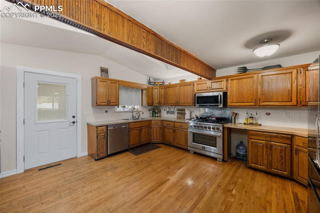 Image 6 of 15: Kitchen with decorative backsplash, light countertops, brown cabinets, ligh
