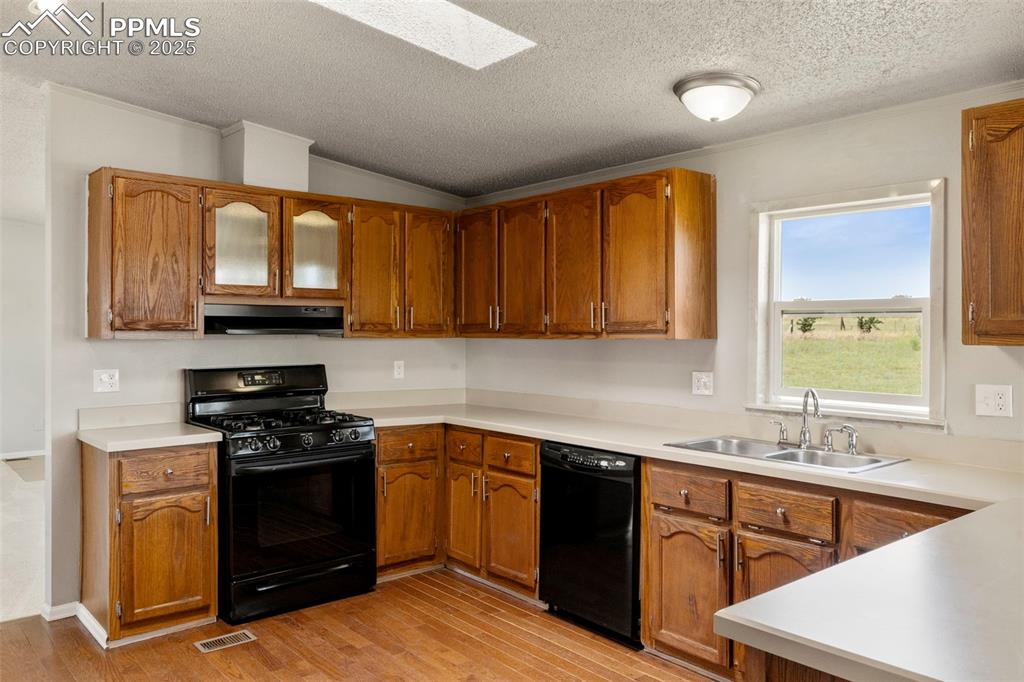 Image 10 of 34: Kitchen with black appliances, under cabinet range hood, a textured ceiling