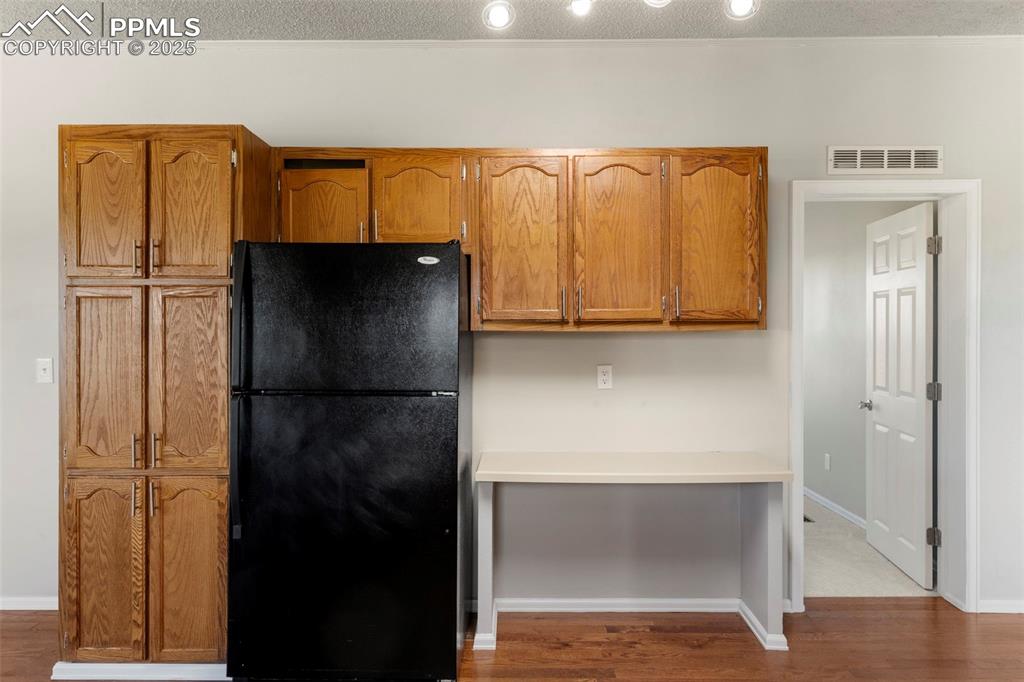 Image 11 of 34: Kitchen with freestanding refrigerator, wood finished floors, brown cabinet