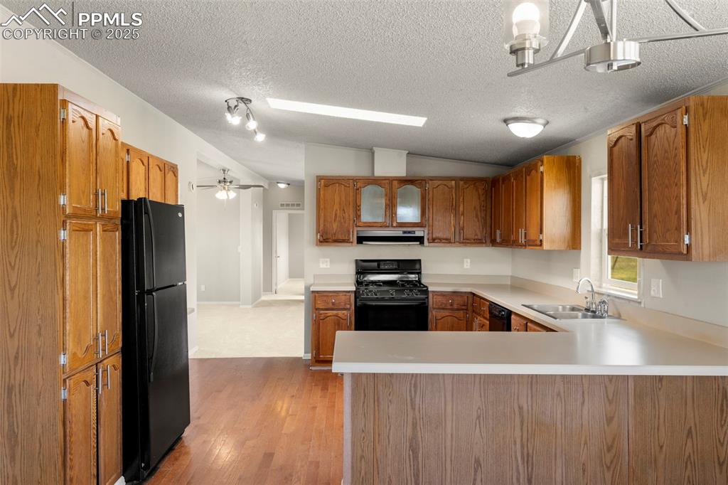 Image 8 of 34: Kitchen with black appliances, under cabinet range hood, vaulted ceiling, a