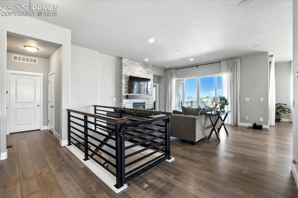 Image 3 of 50: Living area with dark wood-style floors, a textured ceiling, and a stone fi