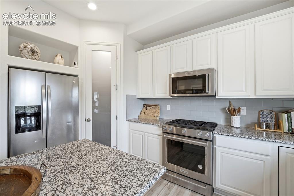 Image 10 of 50: Kitchen featuring white shaker cabinetry, stainless steel appliances, grani