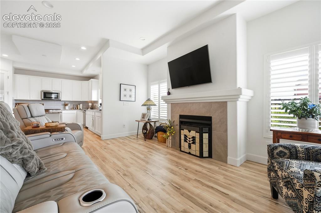 Image 14 of 50: Living area with LVP flooring and a fireplace with a tile surround and mant